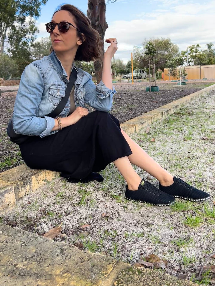 Woman sitting outdoors wearing a denim jacket and black shoes.