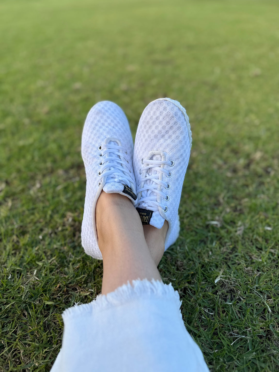 White Corrida sneakers on a person's feet with a grassy background